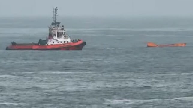 container floating in ocean with tugboat 