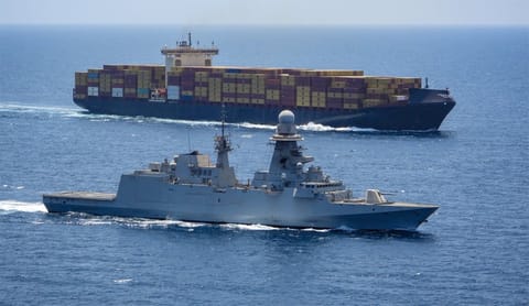 warship sailing alongside containership in the Red Sea