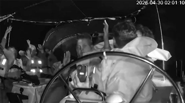 people on boat with lifejackets and hands up