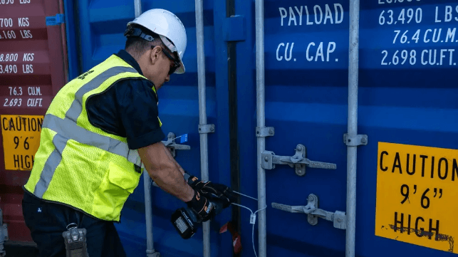 A Coast Guard marine science technician opens a suspect container for inspection (USCG)