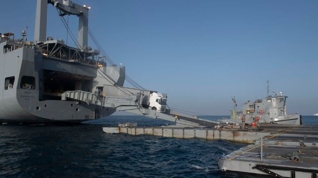 A sealift ship offloads trucks with aid cargoes at a receiving barge off Gaza, May 2024 (USN)