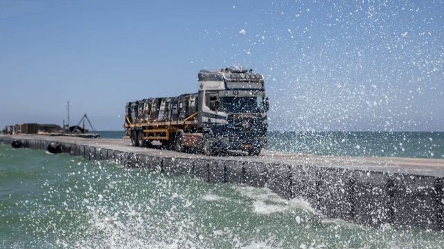 A truck rolls down the floating causeway in modest swells, June 11 (U.S. Army)
