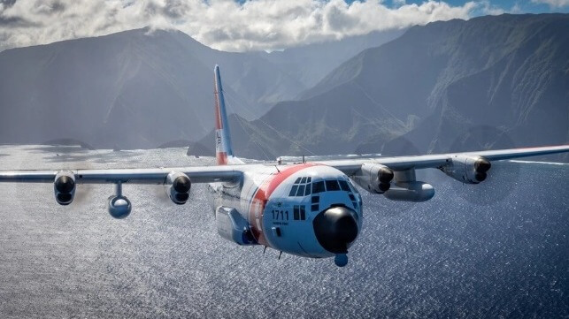 Coast Guard HC-130J long-range SAR aircraft over water with a rugged coastline in background