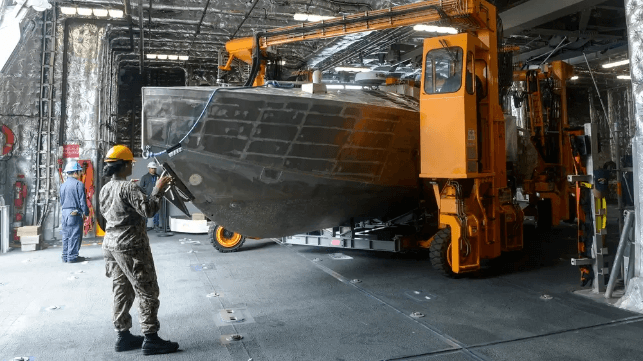 Sailors use a straddle carrier to load a minehunting USV sonar tow vessel aboard USS Canberra, 2024 (USN)