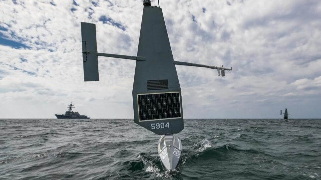 Bow of a Saildrone with a destroyer and another Saildrone in the background