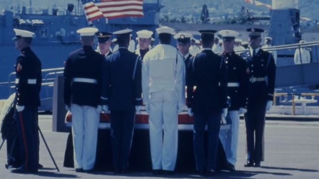 A military honor guard attends the casket of a fallen soldier with a U.S. flag in the background