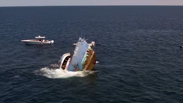 Decommissioned working vessel sinking in blue water with bow in the air