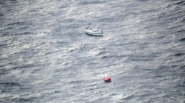 Damaged yacht in the North Atlantic with an inflatable liferaft nearby