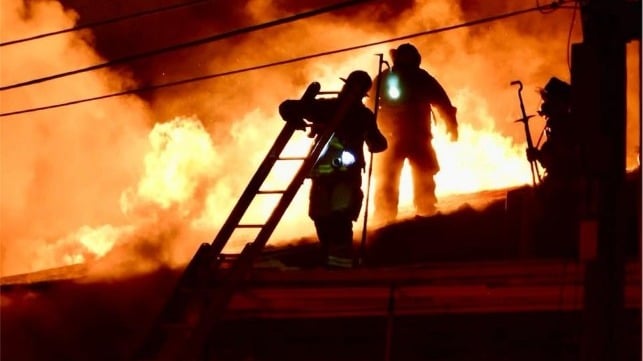 Firefighters climb atop one of the burning buildings in an attempt to control the blaze (PMFD)